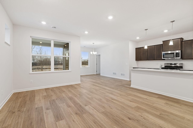 unfurnished living room with an inviting chandelier and light hardwood / wood-style floors