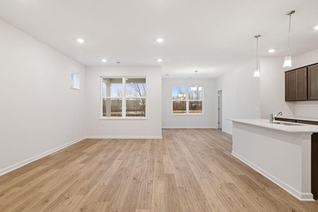 unfurnished living room with an inviting chandelier, sink, and light hardwood / wood-style flooring