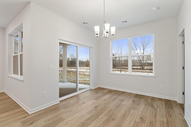 unfurnished dining area with an inviting chandelier and light wood-type flooring