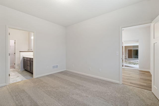 unfurnished bedroom with ensuite bath and light colored carpet