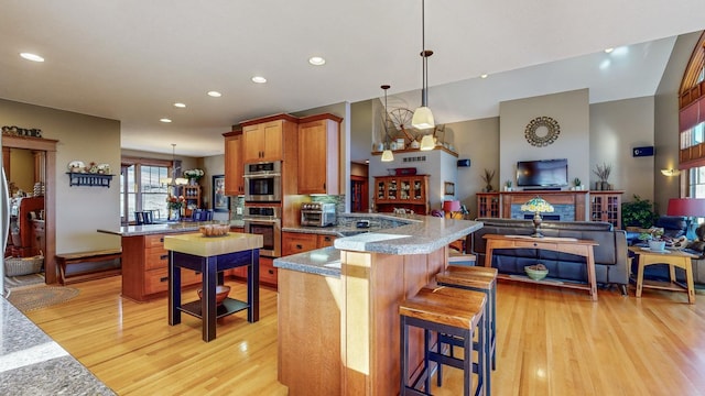 kitchen with a breakfast bar area, kitchen peninsula, hanging light fixtures, and light hardwood / wood-style flooring