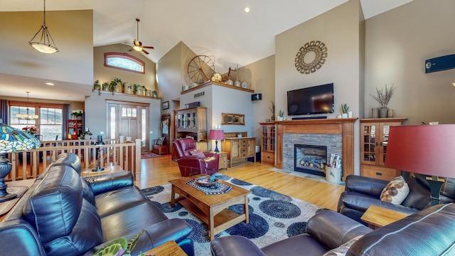 living room with ceiling fan, high vaulted ceiling, a stone fireplace, and light hardwood / wood-style floors