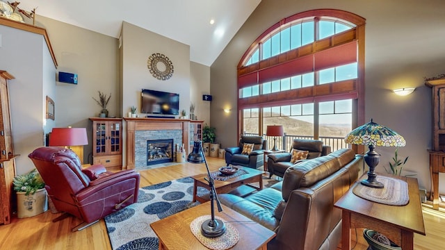 living room featuring hardwood / wood-style flooring, a stone fireplace, and high vaulted ceiling