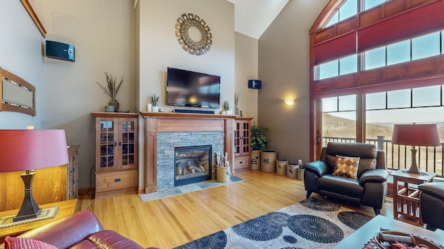 living room featuring plenty of natural light, a stone fireplace, wood-type flooring, and a high ceiling