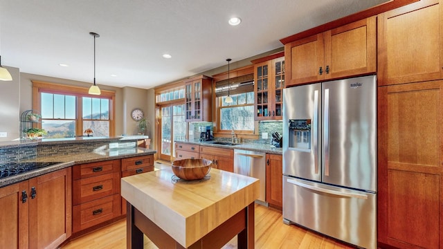 kitchen featuring appliances with stainless steel finishes, pendant lighting, sink, light stone counters, and light hardwood / wood-style flooring