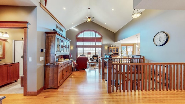 hallway with high vaulted ceiling and light hardwood / wood-style flooring