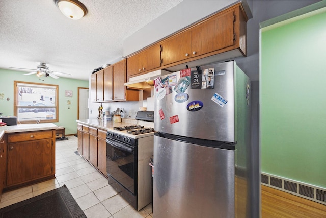 kitchen with light tile patterned flooring, a textured ceiling, stainless steel refrigerator, ceiling fan, and gas range oven