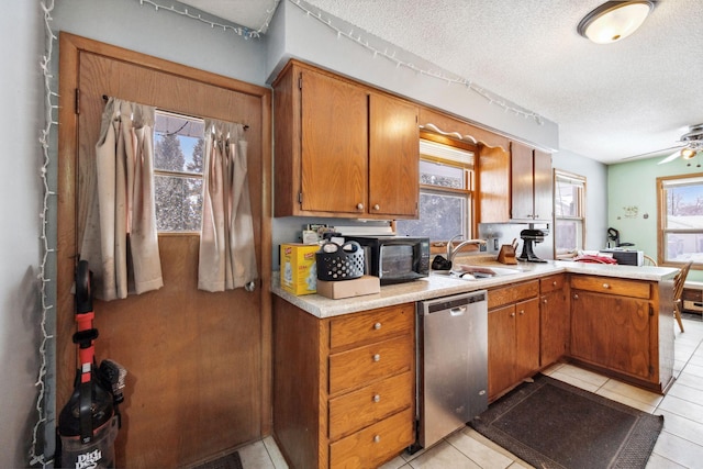 kitchen with sink, a textured ceiling, light tile patterned floors, stainless steel dishwasher, and kitchen peninsula