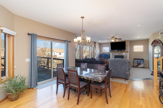 dining room with a healthy amount of sunlight, ceiling fan with notable chandelier, a tile fireplace, and light wood-type flooring