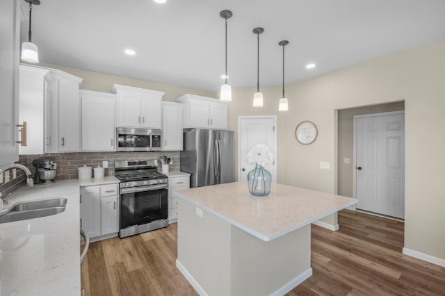 kitchen with a kitchen island, appliances with stainless steel finishes, white cabinetry, sink, and hanging light fixtures