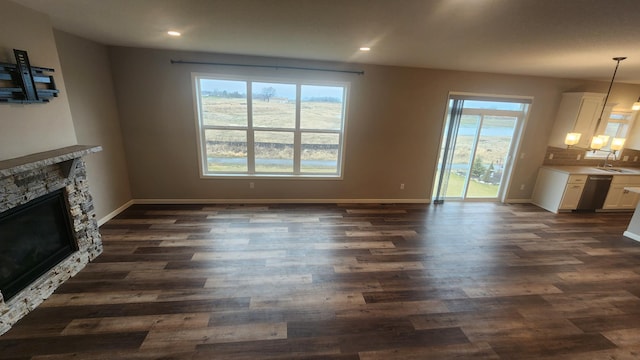 unfurnished living room featuring sink, a stone fireplace, and dark wood-type flooring