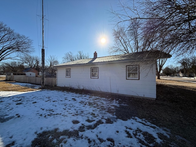 view of snowy exterior featuring a chimney and fence
