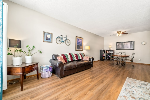 living area featuring light wood-style floors, ceiling fan, baseboards, and a textured ceiling