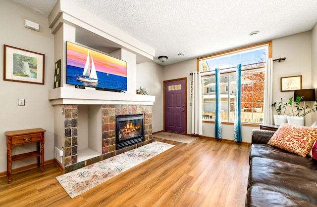 living room featuring a textured ceiling, a tiled fireplace, wood finished floors, and baseboards