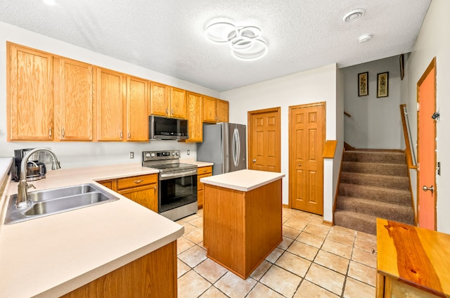 kitchen with light countertops, appliances with stainless steel finishes, a kitchen island, a textured ceiling, and a sink