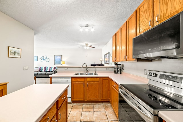 kitchen with brown cabinetry, appliances with stainless steel finishes, a peninsula, light countertops, and a sink