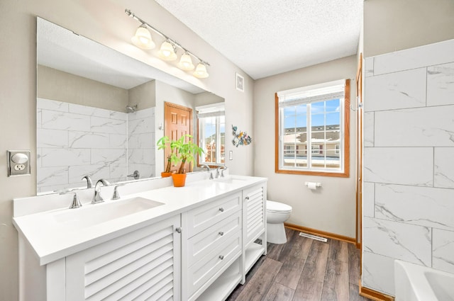 full bath with a textured ceiling, wood finished floors, a sink, visible vents, and double vanity