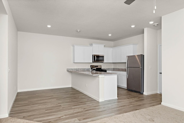 kitchen with appliances with stainless steel finishes, white cabinetry, kitchen peninsula, light stone countertops, and light wood-type flooring