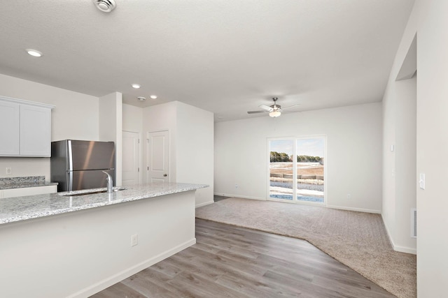 kitchen featuring sink, stainless steel refrigerator, ceiling fan, light stone counters, and white cabinets