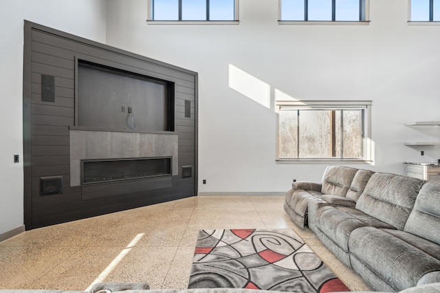 living area featuring a large fireplace, a healthy amount of sunlight, baseboards, and a high ceiling