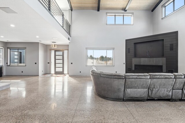 living room featuring a towering ceiling, speckled floor, plenty of natural light, and beam ceiling