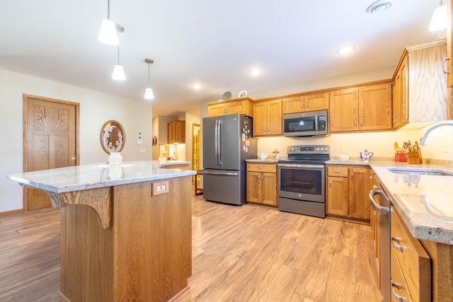 kitchen with appliances with stainless steel finishes, a sink, light wood-style floors, a center island, and light stone countertops