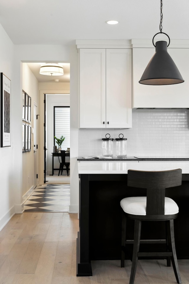 kitchen with white cabinetry, decorative backsplash, hanging light fixtures, and light hardwood / wood-style flooring