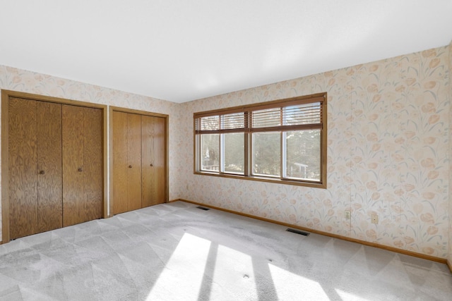 unfurnished bedroom featuring multiple closets and light colored carpet