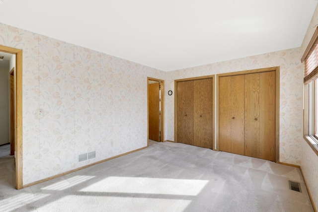 unfurnished bedroom with two closets and light colored carpet