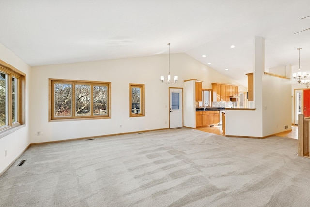 unfurnished living room featuring light colored carpet, a notable chandelier, a sink, visible vents, and baseboards