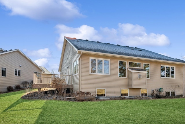 rear view of house featuring roof with shingles, a yard, and a deck