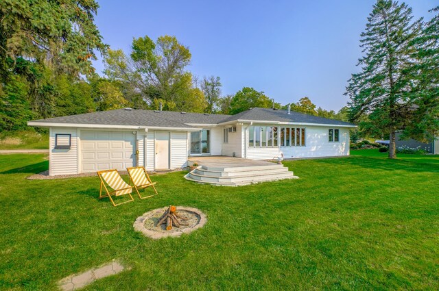 rear view of property with a lawn, a deck, an outdoor fire pit, and a garage