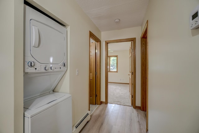 laundry room featuring a baseboard radiator, stacked washer / dryer, light wood-type flooring, baseboards, and laundry area