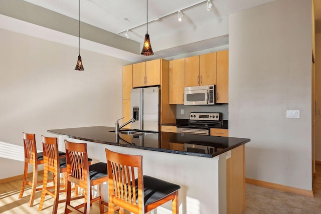 kitchen with appliances with stainless steel finishes, light brown cabinetry, sink, dark stone countertops, and hanging light fixtures