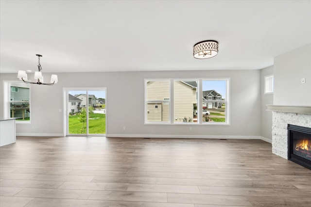 unfurnished living room featuring plenty of natural light, an inviting chandelier, a fireplace, and light hardwood / wood-style flooring