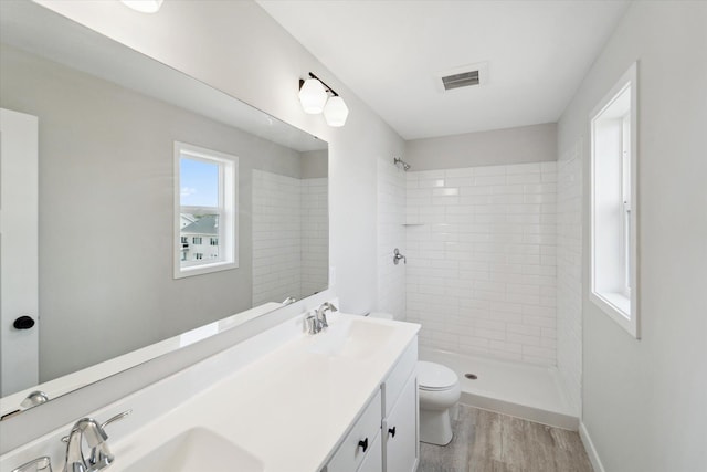 bathroom featuring a tile shower, hardwood / wood-style floors, vanity, and toilet