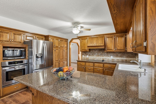 kitchen with sink, a textured ceiling, kitchen peninsula, stainless steel appliances, and backsplash