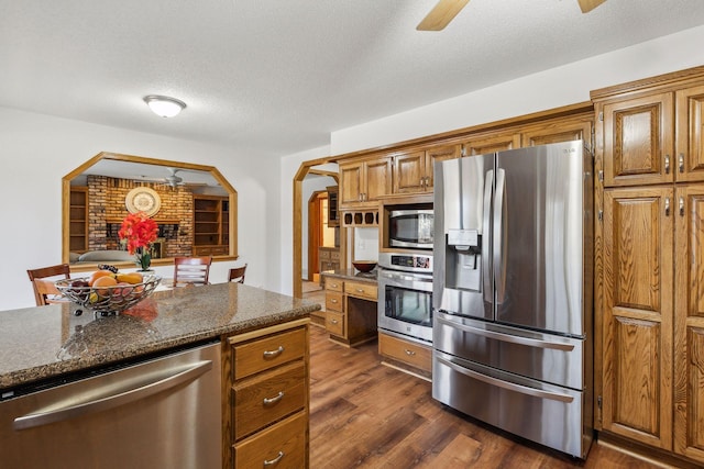 kitchen featuring a textured ceiling, dark stone countertops, appliances with stainless steel finishes, dark hardwood / wood-style floors, and ceiling fan