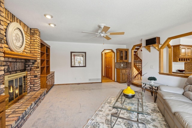 living room featuring light carpet, ceiling fan, a fireplace, and a textured ceiling