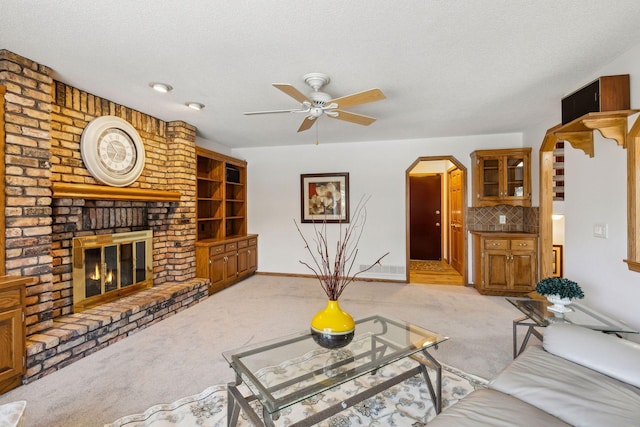 living room with ceiling fan, a fireplace, light colored carpet, and a textured ceiling