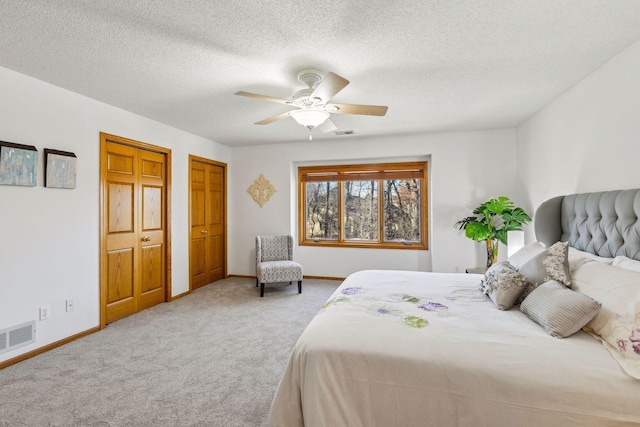 carpeted bedroom featuring ceiling fan, a textured ceiling, and two closets