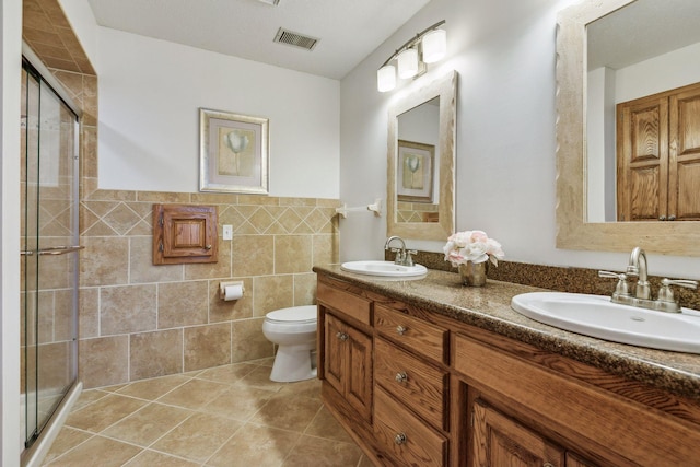 bathroom with a shower with shower door, tile walls, tile patterned flooring, vanity, and toilet