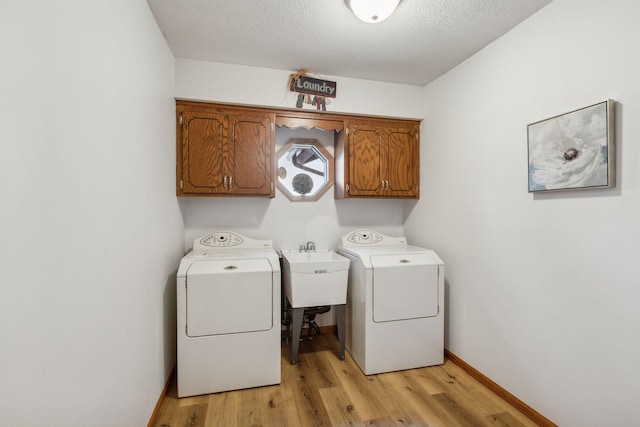 clothes washing area featuring sink, cabinets, washing machine and dryer, a textured ceiling, and light hardwood / wood-style flooring