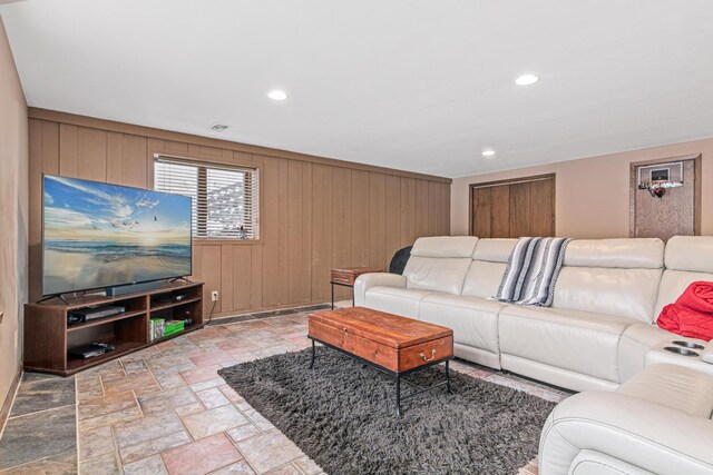 living area featuring recessed lighting, stone finish flooring, visible vents, and wooden walls