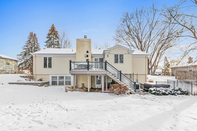 snow covered property with stairway, a chimney, and a deck