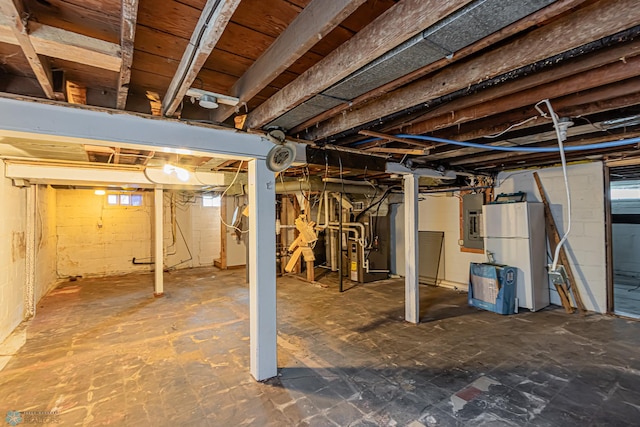 basement featuring heating unit, electric panel, and white refrigerator