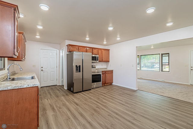 kitchen featuring stainless steel appliances, light stone countertops, sink, and light hardwood / wood-style flooring