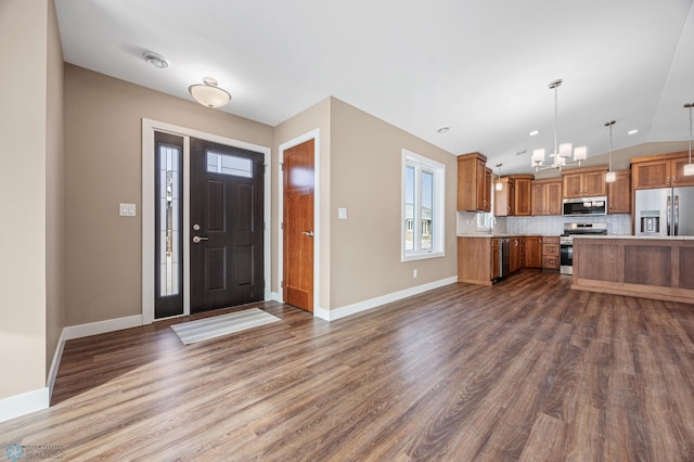 kitchen featuring dark wood-type flooring, decorative backsplash, appliances with stainless steel finishes, and hanging light fixtures