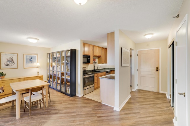 kitchen with stainless steel appliances, dark countertops, a sink, and light wood-style floors