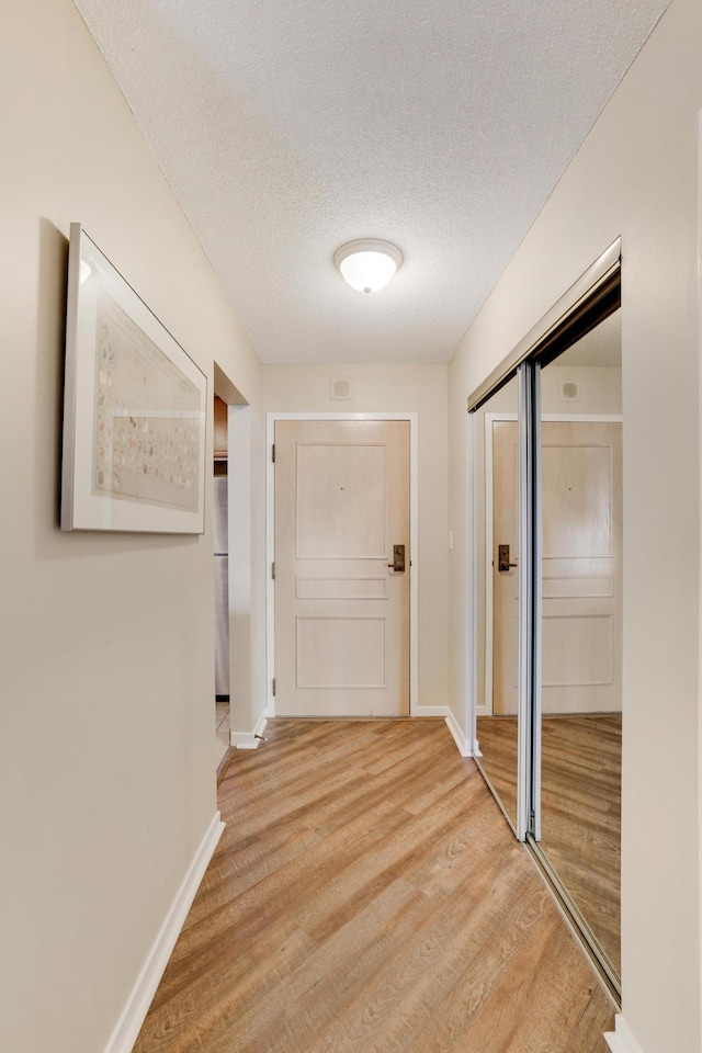 hall with a textured ceiling, light wood-type flooring, and baseboards